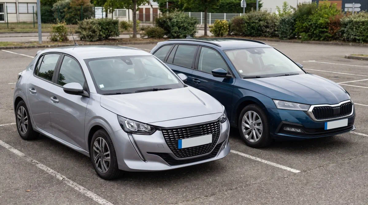 Une citadine grise et un break bleu garés côte à côte sur un parking.